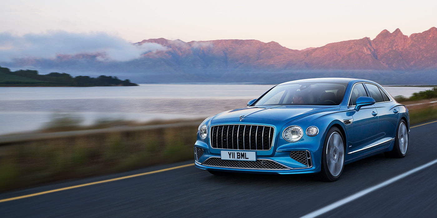 Feser-Graf Exclusive Cars GmbH | Bentley Nürnberg New Bentley Flying Spur Azure sedan in Light windsor blue paint by Mulliner, with 22 inch Azure wheels and chrome straight vaned grille driving on a mountain road