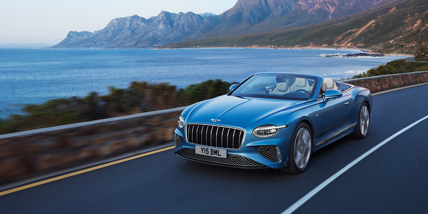 Feser-Graf Exclusive Cars GmbH | Bentley Nürnberg New Bentley Continental GTC Azure convertible in Light Windsor blue paint with 22 inch Azure wheels and chrome grill, driving dynamically by the sea