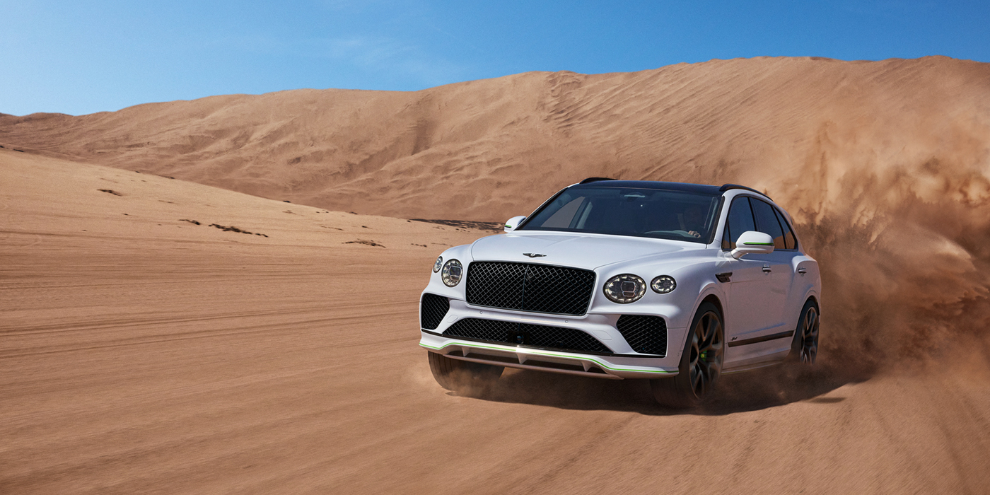 Feser-Graf Exclusive Cars GmbH | Bentley Nürnberg Bentley Bentayga Speed SUV front three quarter in Snow Quarts Pearlescent by Mulliner white paint driving dynamically through the desert