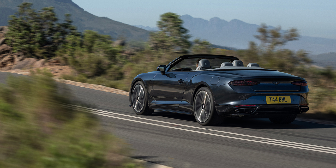 Feser-Graf Exclusive Cars GmbH | Bentley Nürnberg Bentley Continental GTC S convertible in Thunder blue paint rear 3/4 driving on mountain road