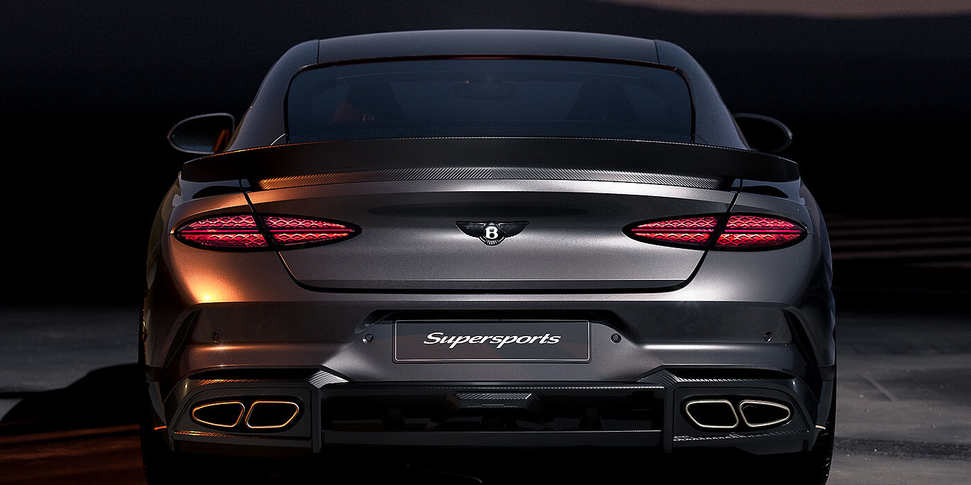 Feser-Graf Exclusive Cars GmbH | Bentley Nürnberg Bentley Supersports rear view with illuminated rear lamps, spoiler and black Bentley badge in Anthracite paint against a dark grey and red background