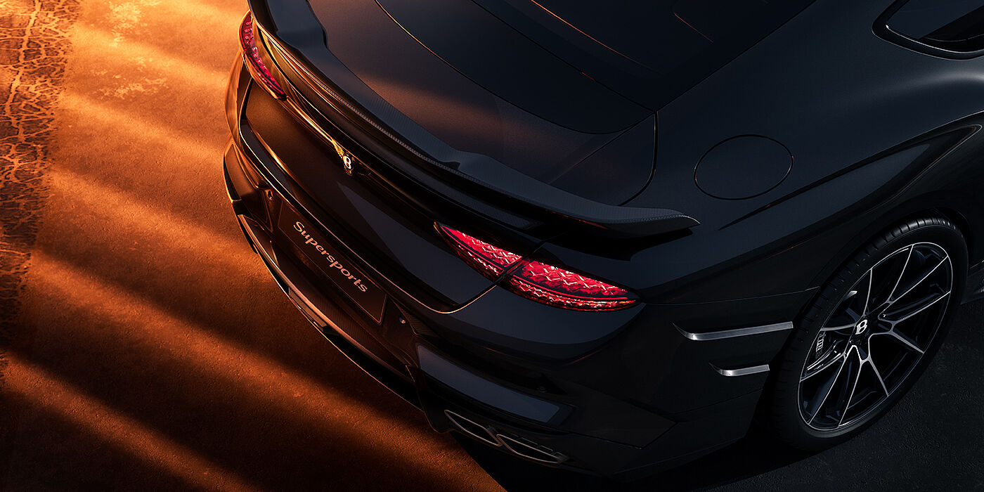 Feser-Graf Exclusive Cars GmbH | Bentley Nürnberg Bentley Supersports rear overhead view showing illuminated rear lamps and Supersports Forged Alloy wheel in Anthracite paint against a dark grey and red background
