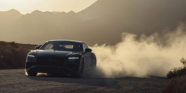 Feser-Graf Exclusive Cars GmbH | Bentley Nürnberg Bentley Continental GT coupe in Thunder paint front 3/4 driving with dust trail at sunset