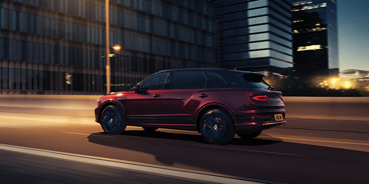 Feser-Graf Exclusive Cars GmbH | Bentley Nürnberg Bentley Bentayga Extended Wheelbase Mulliner SUV in Cricket Ball red paint driving dynamically in city at night